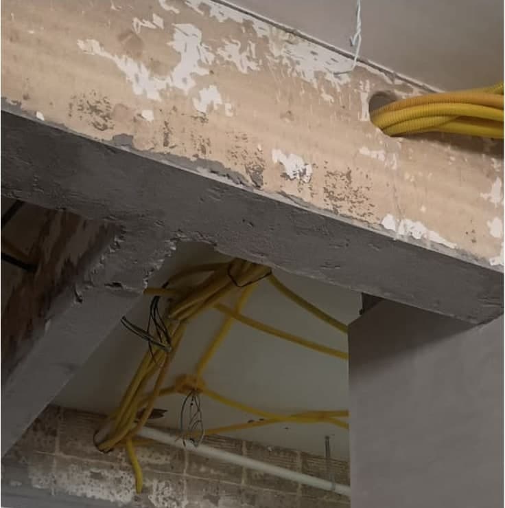 Furo em viga de concreto com eletroduto amarelo passando próximo ao teto